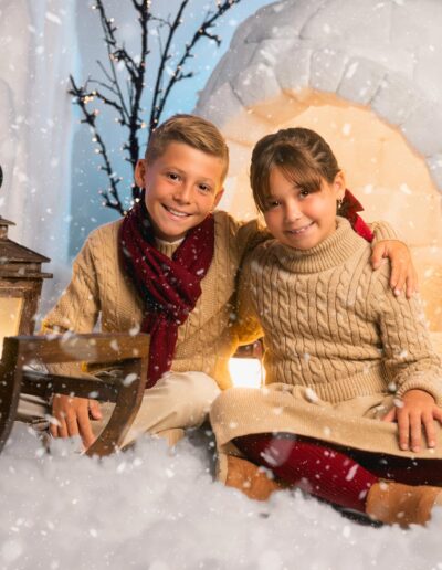 Dos hermanos abrazados delante del iglú navideño
