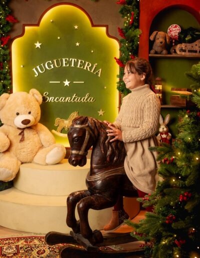 Niña jugando junto al caballo de madera del decorado navideño