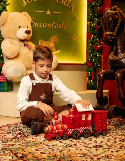 Niño sentado junto al oso de peluche y el caballo de madera navideño